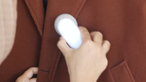 cleaning a brown wool coat with a lint roller