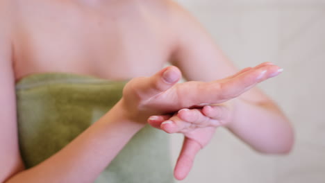close-up view of woman in green towel gently rubbing cream on hand after shower, focusing on post-shower skincare routine, moisturizing dry skin in quiet bathroom setting for self-care and wellness