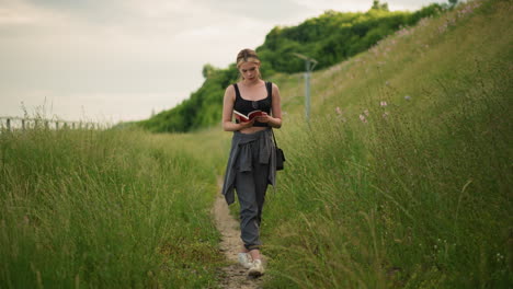 woman walking along a grassy path while reading a book, surrounded by tall green grass and a calm outdoor environment, focused on her book, blending nature with the peaceful act of reading