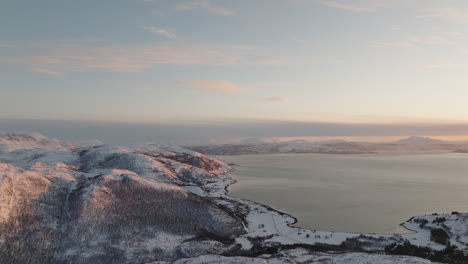 aerial view of fjord, kvaloya island with forest covered with snow at sunset in norway