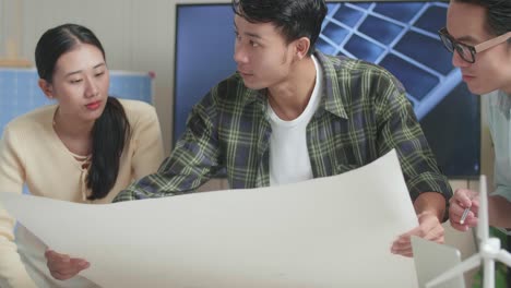 primer plano de un grupo de ingenieros asiáticos con el modelo de la casa de paneles solares discutiendo sobre el trabajo en el plano en manos en la oficina