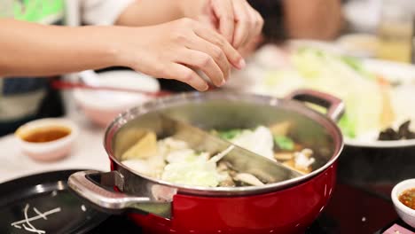 hands adding ingredients to a hotpot