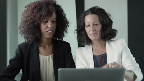 Two serious businesswomen sitting together and talking in front of their laptops