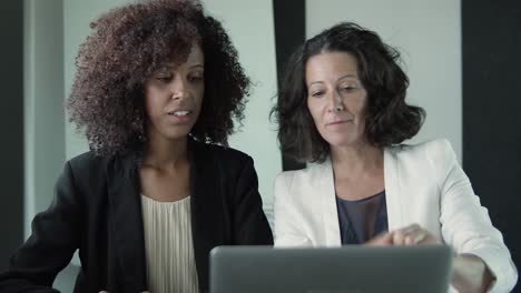 two serious businesswomen sitting together and talking in front of their laptops