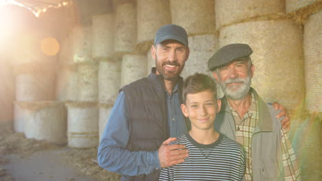 teen boy with her father and grandfather standing in stable with hay stocks and smiling at camera