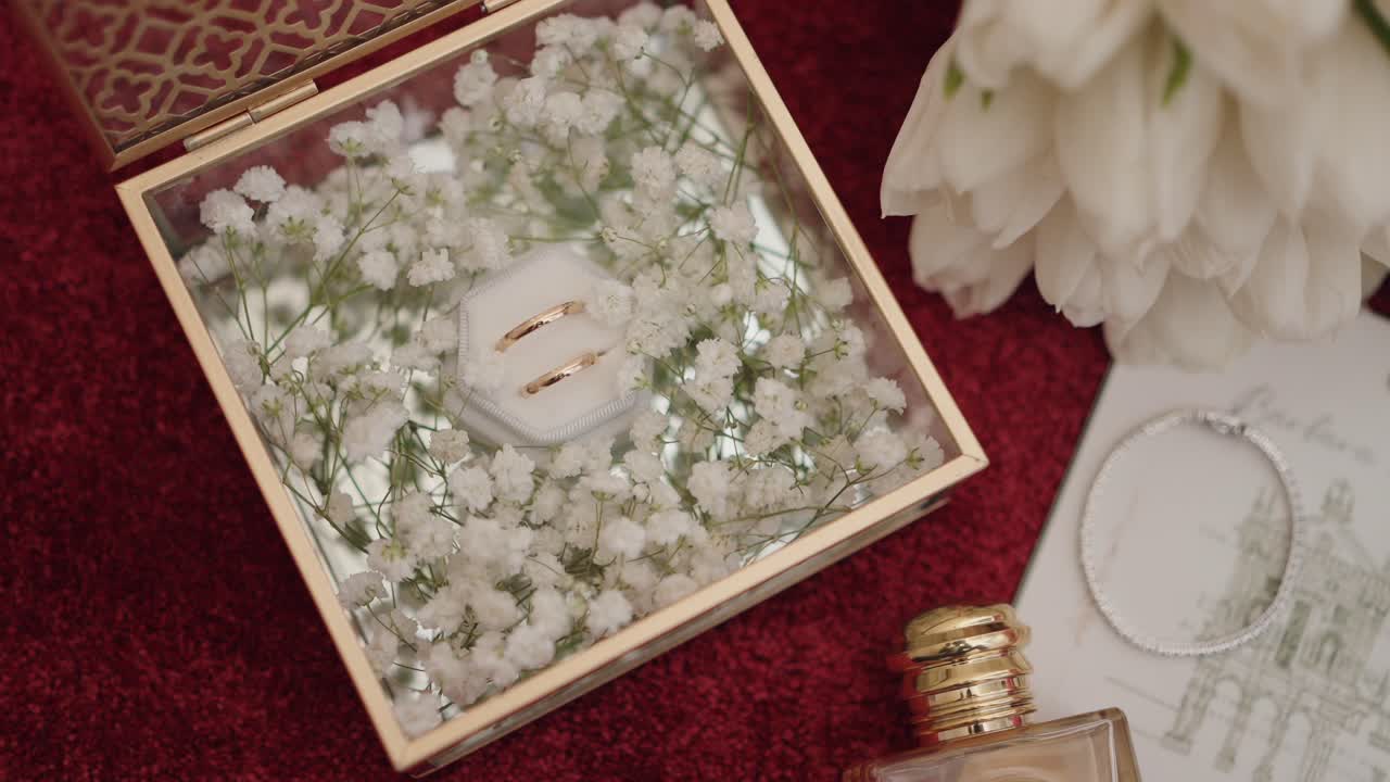 closeup of wedding rings in a floral glass box with perfume and flowers