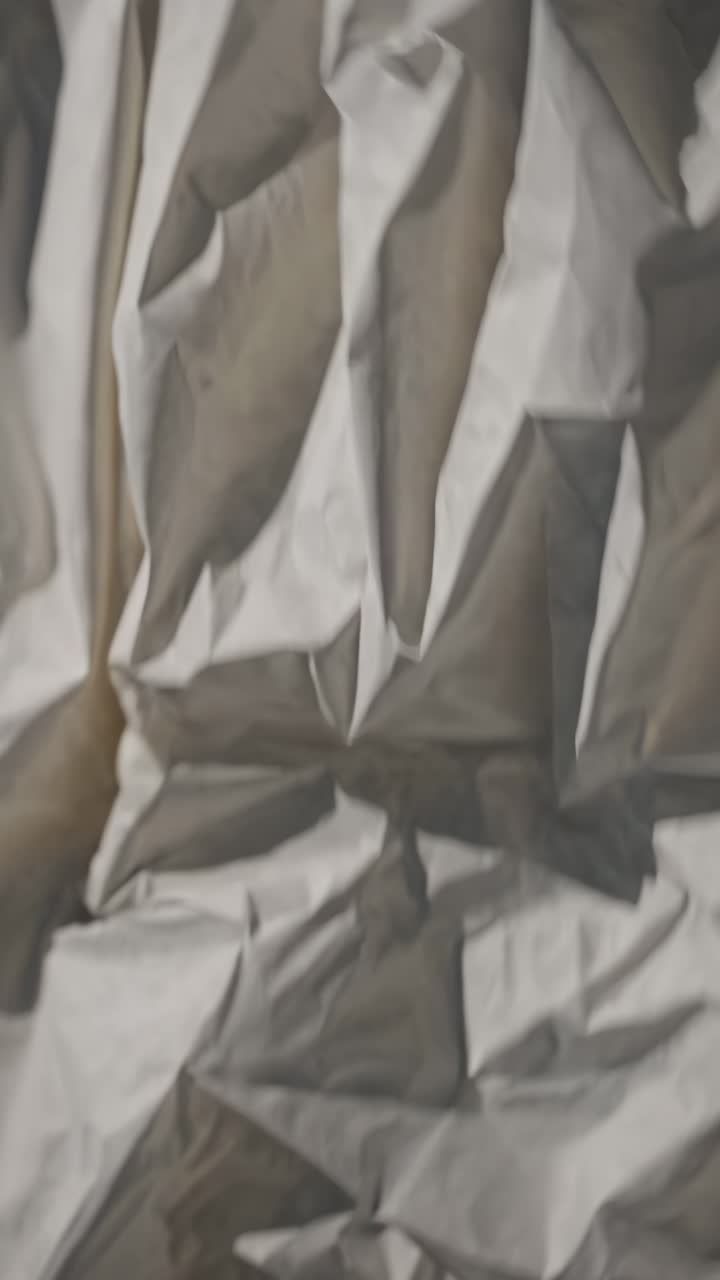 Close-up video of crumpled paper texture, showcasing intricate folds and shadows