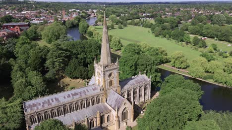 Aerial-view-across-lush-green-rural-Warwickshire-countryside-descending-Holy-Trinity-church-spire