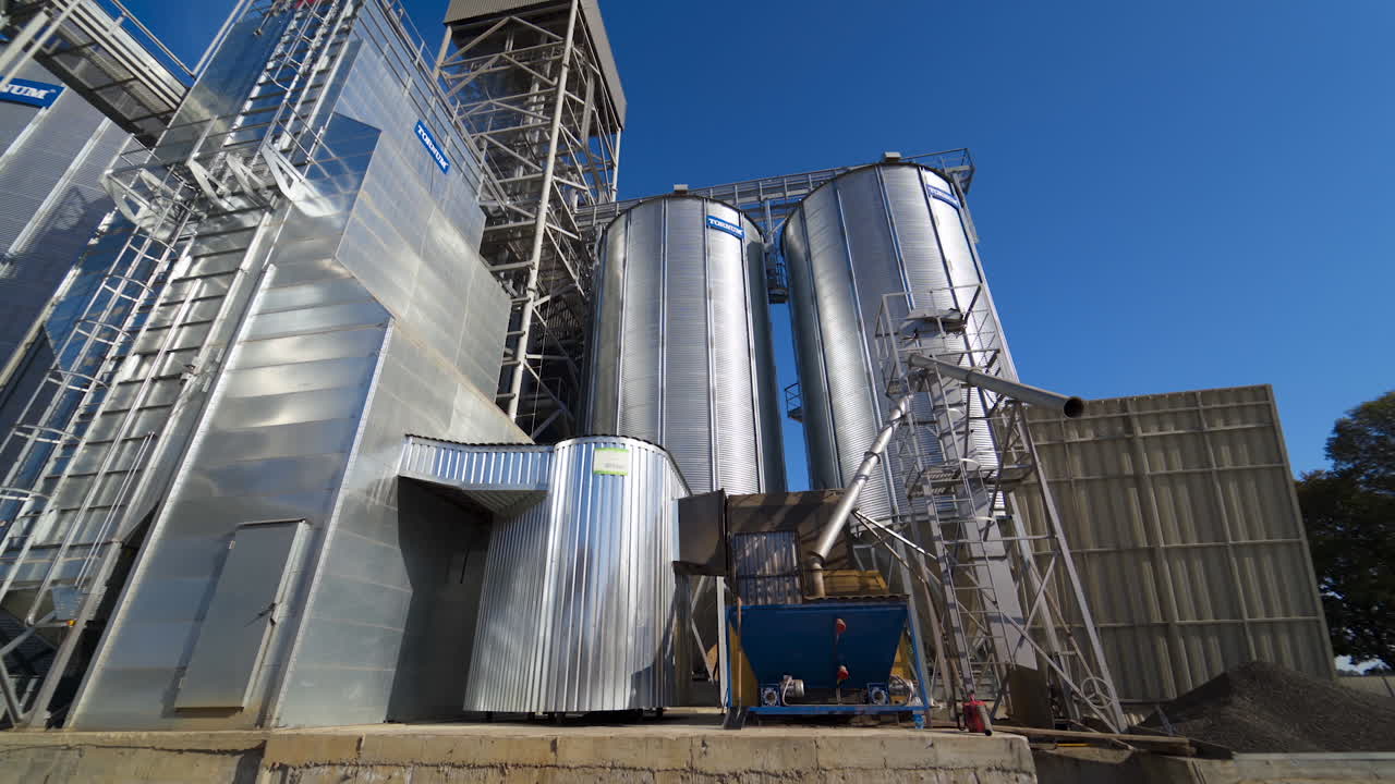 Metal grain elevator in agricultural zone. Silver silos on agro manufacturing plant for processing drying cleaning and storage of agricultural products