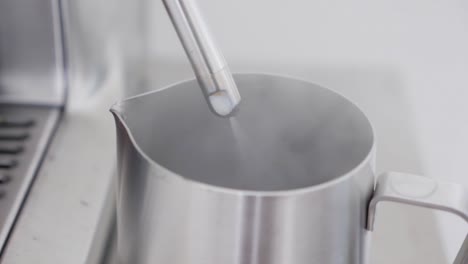 Medium-slow-motion-shot-of-a-steaming-wand-purging-water-getting-ready-to-steam-milk