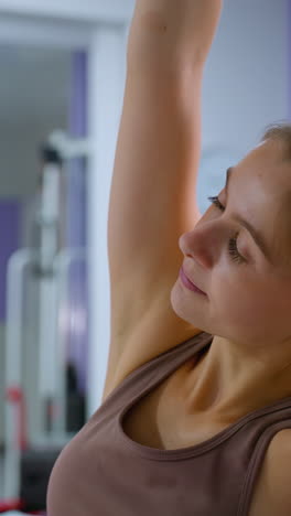dos mujeres participan en una rutina de fitness sincronizada, levantando rodillos de espuma por encima y estirándose lateralmente, con un gran espejo que refleja sus movimientos en un entorno de gimnasio moderno