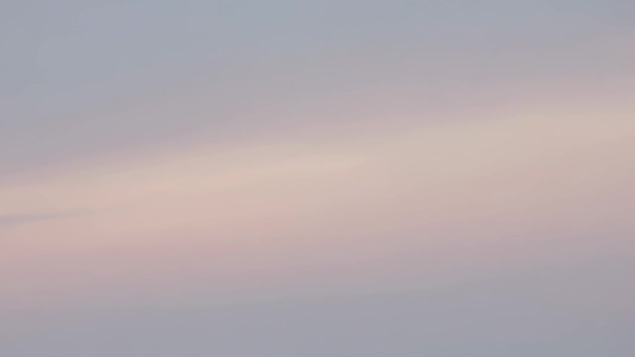Centreret pastelfarvet himmel skifter under solopgangens lysskifte, med et tyndt lyserødt skybånd.
