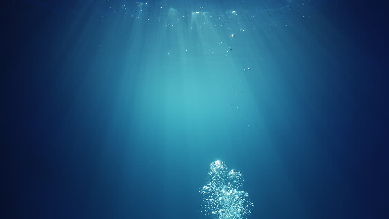 위에서부터 빛나는 수중 햇빛 광선이 깊고 맑고 푸른 물을 통과하여 수면 위로 올라오는 기포가 있는 아름다운 물 조명 반사 커튼을 만듭니다.