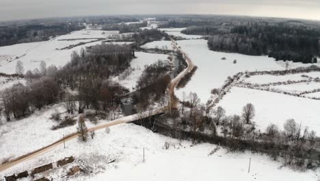 aerial drone shot of a small bridge over a river in countryside with empty gravel road. cloudy winter day.