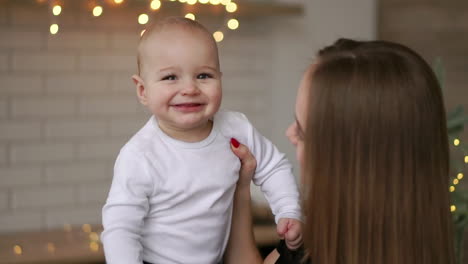 mother and her baby son having fun and playing at home. little kid 2 years old play with his mom arms at home near a big window