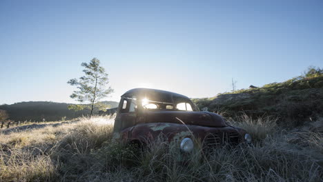 derelict truck in a grassy hill pan time-lapse with sun rising in the background