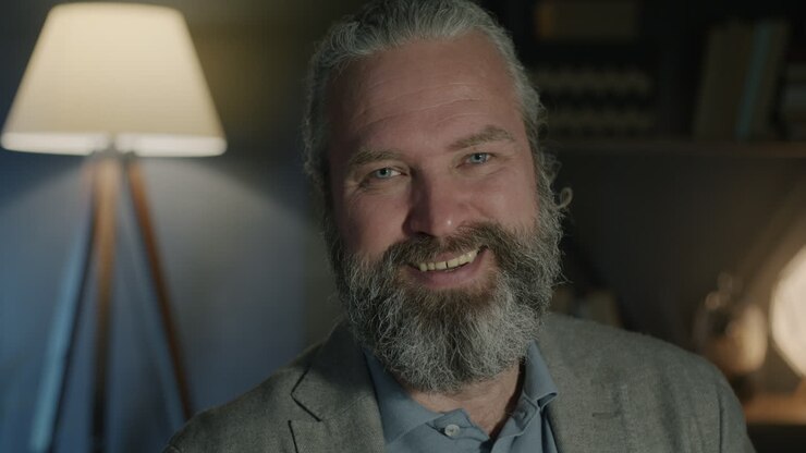 Smilende mand med gråt hår og skæg i hjemlige omgivelser