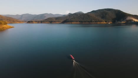 Traditionelles-Thailändisches-Boot-Segelt-Mit-Hoher-Geschwindigkeit-über-Den-Wunderschönen-Mae-Ngat-Somboon-Im-Srilanna-Nationalpark-Mit-Bäumen,-Die-Von-Den-Sonnenuntergangsfarben-Beleuchtet-Werden