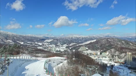 aerial - rising drone shot from peak of snowy ski resort on sunny day