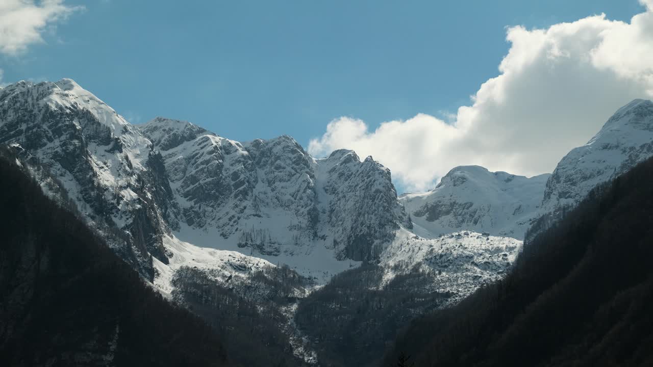 Thick white clouds flowing over snow-covered mountain tops, timelapse