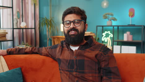 portrait of happy indian man looking at camera and smiling at home relaxing wearing eyeglasses