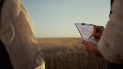 los socios firman un contrato en el campo de trigo. las manos de los agricultores sostienen el clipboard de cerca.