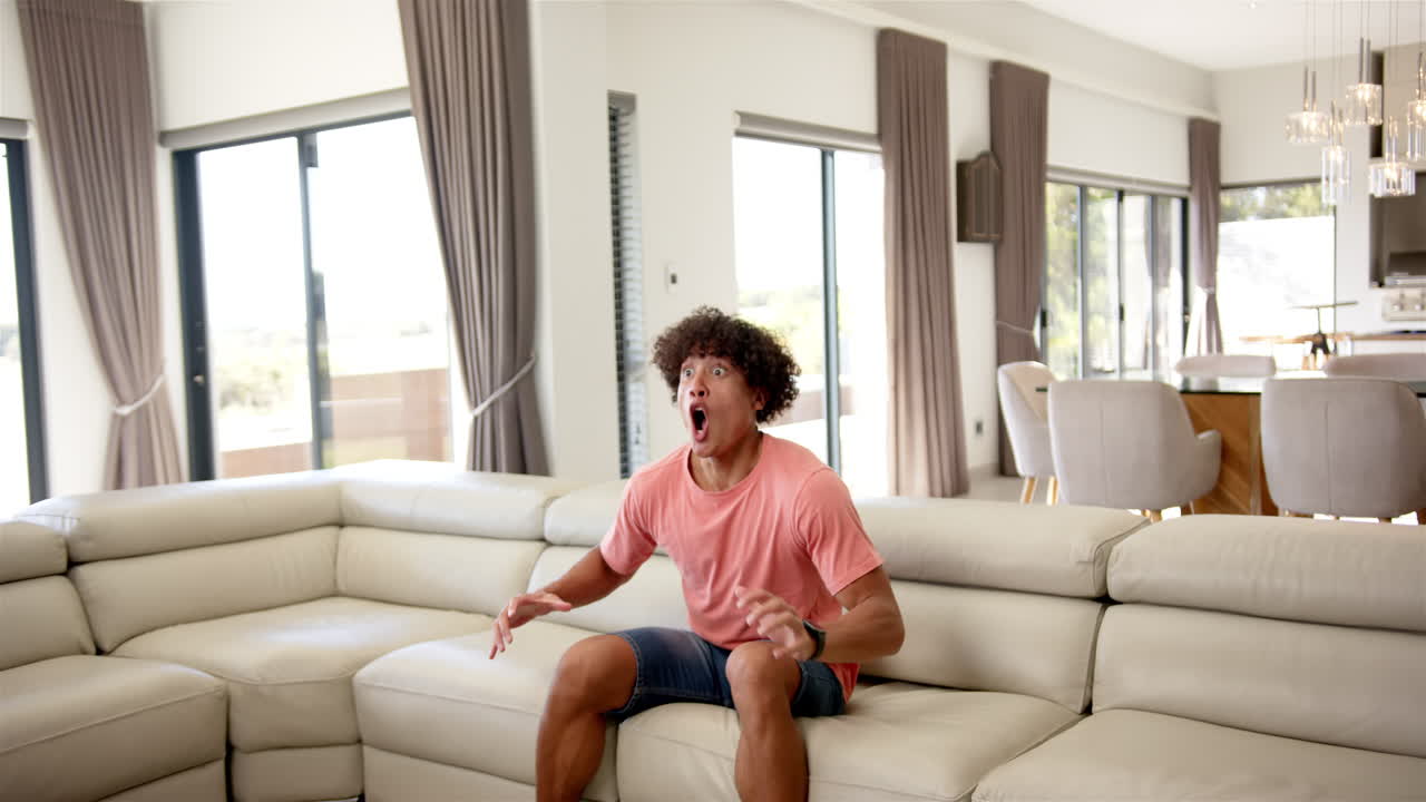 Excited man in casual clothes jumping on couch in modern living room