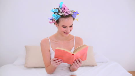 joven modelo en rodillos de cabello leyendo un libro en su cama