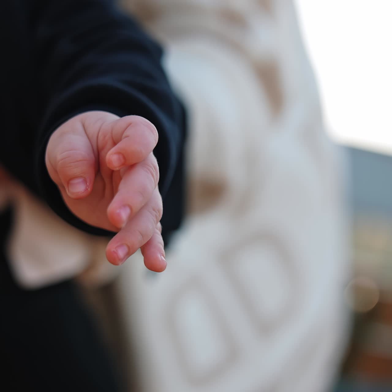 Hands of a little baby wearing black sweater. Close up. Child in mom's hands close up