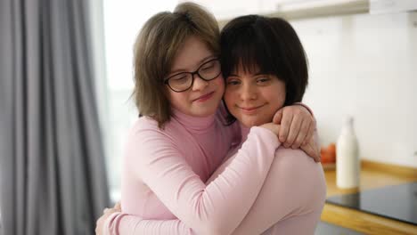 Zwei-Süße-Mädchen-Mit-Down-Syndrom-Stehen-Zusammen-Und-Umarmen-Sich-Zu-Hause
