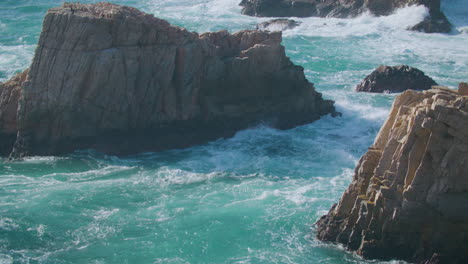 pan hacia abajo desde las rocas dentadas en los pintores apuntan a un león marino tomando el sol en medio de olas agitadas