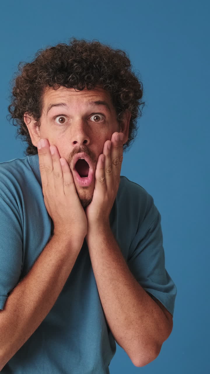 Joven expresando asombro y sorpresa sobre fondo azul
