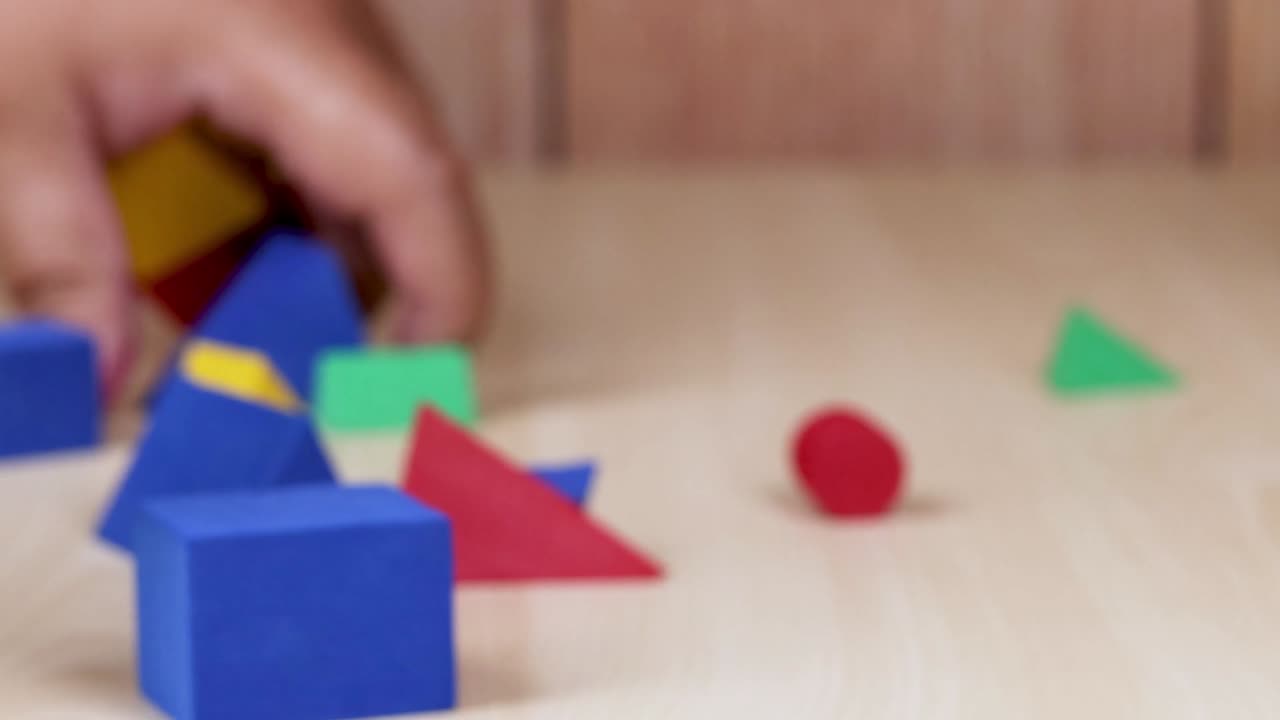 Hands arranging and stacking colorful geometric foam shapes on a wooden surface.