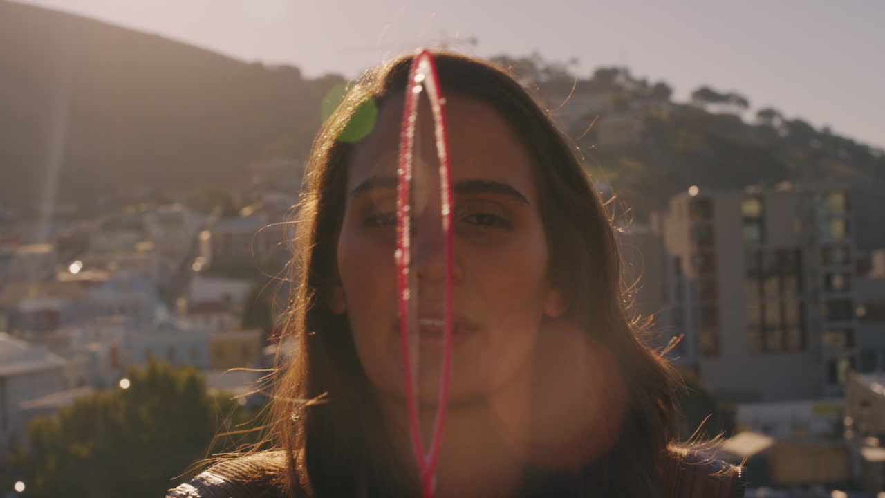 hermosa mujer caucásica soplando burbujas en el techo al atardecer disfrutando de un divertido día de verano con la ciudad en el fondo