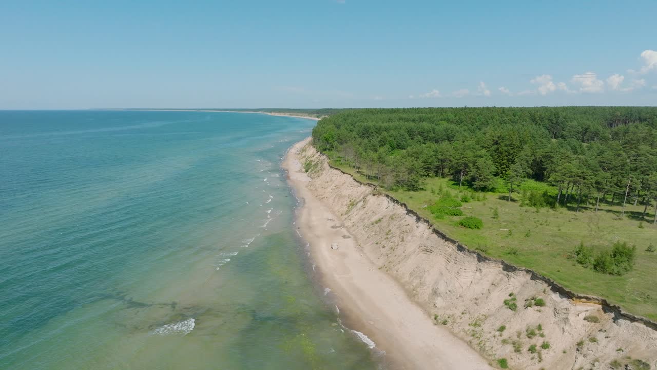 Aerial establishing view of Baltic sea beach at Jurkalne on a sunny summer day, white sand cliff damaged by waves, coastal erosion, climate changes, wide drone shot moving forward