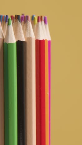 disparo vertical de estudio de vídeo de lápices giratorios multicolores contra un fondo amarillo