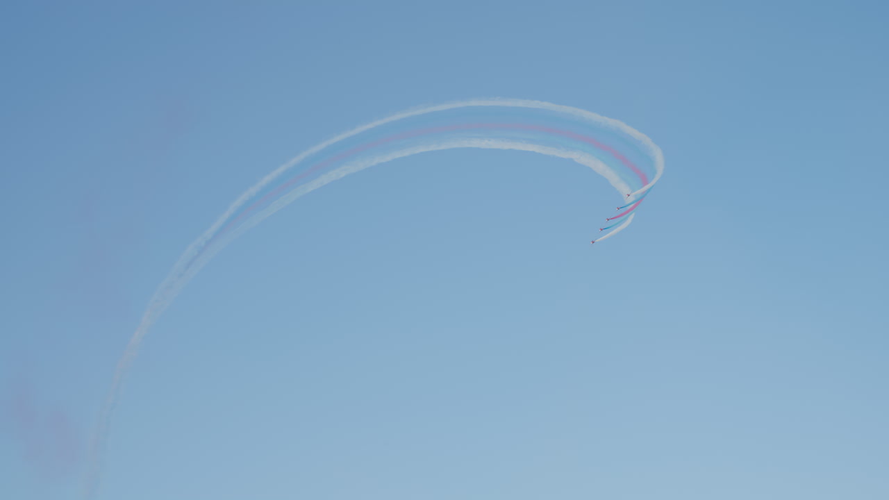 Aerei rossi che eseguono acrobazie aeree con scie di fumo colorato nel cielo blu