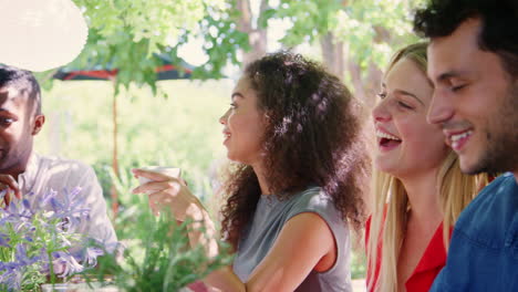 jóvenes amigos adultos sentados en una mesa en un jardín riendo