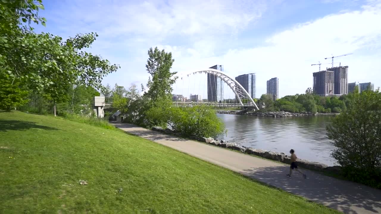 jogger corre a lo largo de la orilla del lago con un puente en el fondo, al lado del lago ontario en el centro de toronto en el verano