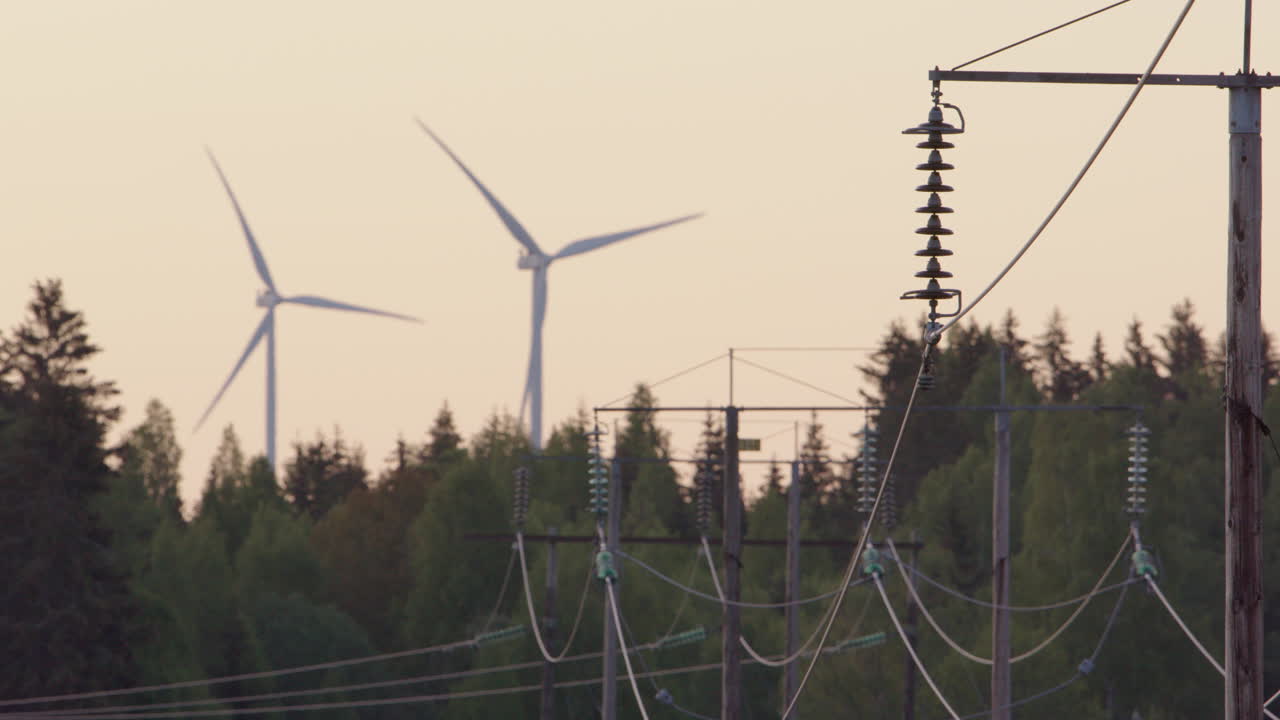 DAWN, GOLDEN HOUR - Wind turbines spin behind electricity cables