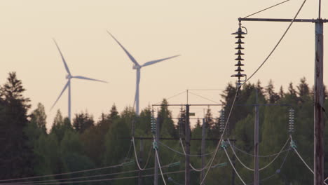 dawn, golden hour - wind turbines spin behind electricity cables