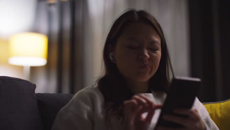 close up of woman spending evening at home on sofa wearing wireless earbuds and streaming music or podcast from mobile phone 2