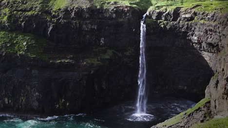 shot of múlafossur waterfall with birds flying and crashing waves against coastline on vagar island, faroe island