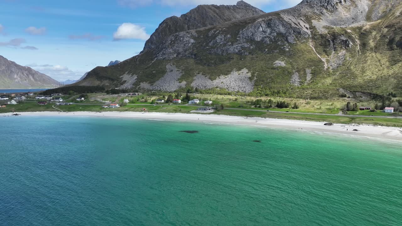 Luftpanorering över vatten med vy nedåt på semesterbostäder längs Ramberg Beach, Flakstad, Lofoten, Norge