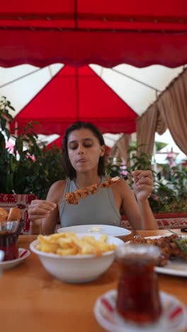 woman eating grilled chicken skewers at an outdoor restaurant