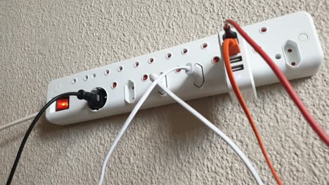 male hand plugging in an electric usb phone and tablet charger into a wall mounted european 220v style multi plug