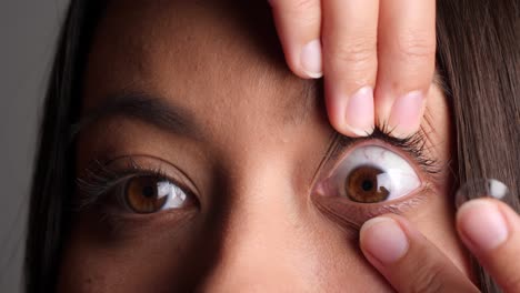 young southeast asian woman inserts contact lens, close-up studio-shot