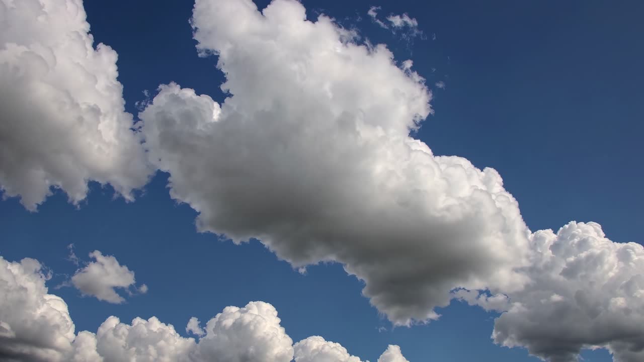 Um vídeo sereno capta nuvens brancas e fofas contra um céu azul profundo, filmado de um ângulo baixo