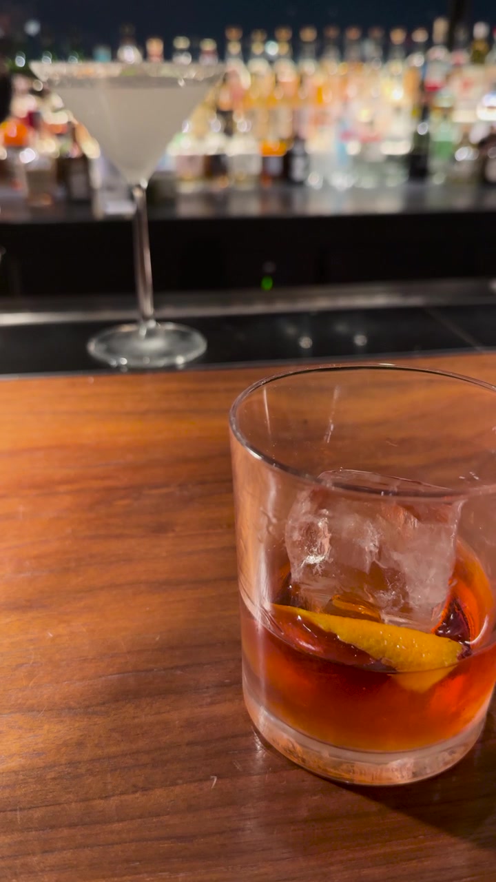 Primo piano di un cocktail ambrato con un grande cubo di ghiaccio e una guarnizione di scorza d'arancia.