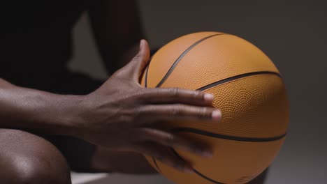 Nahaufnahme-Eines-Sitzenden-Männlichen-Basketballspielers-Mit-Händen,-Die-Ball-1-Halten